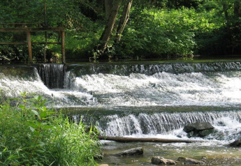 Kleine waterval en weelderige begroeiing langs een rivier, gefotografeerd nabij een safaritent.