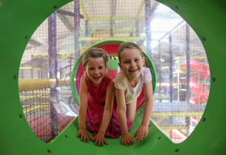 Two happy children playing inside an indoor play center, smiling while crawling in a green tunnel.