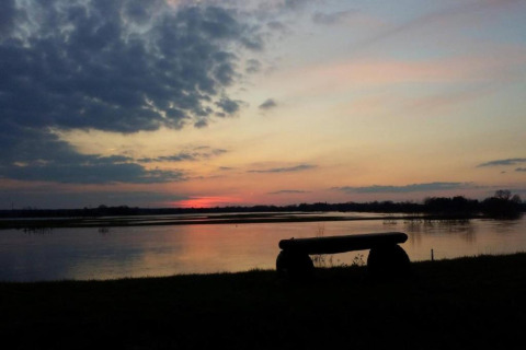 Stunning sunset over a river as seen from a safari tent camp, with a bench silhouetted in front.