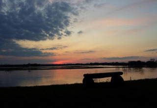 Stunning sunset over a river as seen from a safari tent camp, with a bench silhouetted in front.