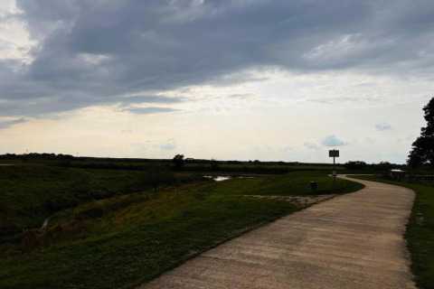 A path winds through open grassland under a cloudy sky near a safari tent camping area.