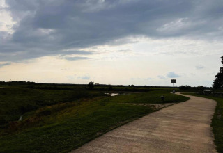 A path winds through open grassland under a cloudy sky near a safari tent camping area.