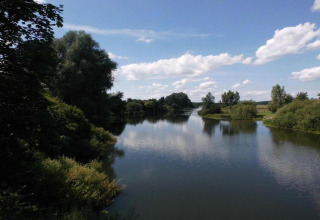 View from a safari tent overlooking a calm river with lush trees and bushes under a blue sky.