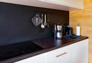 Modern kitchen countertop at Haus Wasser in Germany featuring coffee maker, stove, and hanging utensils.