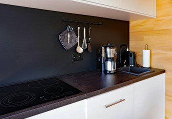 Modern kitchen countertop at Haus Wasser in Germany featuring coffee maker, stove, and hanging utensils.