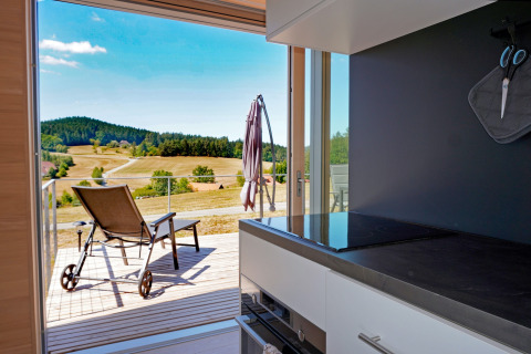 View from the kitchen at Haus Wasser, Germany, overlooking a sunny terrace and scenic rural hills.