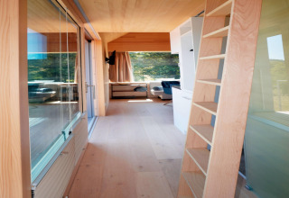 Interior view of Haus Wasser cabin in Germany featuring wood ladder, large windows, and minimalist decor.