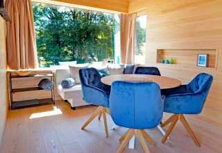 Modern living room at Haus Wasser, Germany, featuring blue chairs, wood table, and large scenic window views.