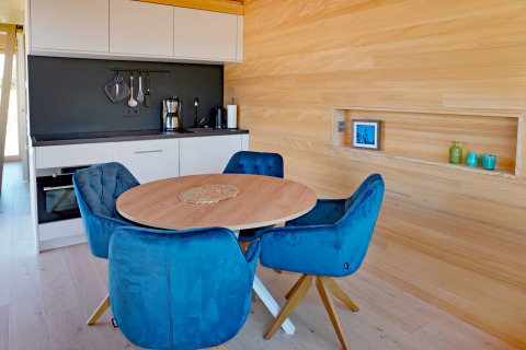 Modern kitchen and dining area in a wooden cabin, featuring blue chairs at Haus Wasser in Germany.