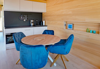 Modern kitchen and dining area in a wooden cabin, featuring blue chairs at Haus Wasser in Germany.
