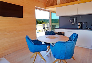 Contemporary cabin interior at Haus Wasser in Germany with blue chairs, round table, and kitchen.