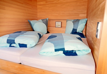 Modern twin bed with blue bedding in a wood-paneled cabin, photographed at Haus Wasser, Germany.