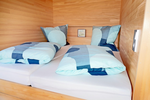 Modern twin bed with blue bedding in a wood-paneled cabin, photographed at Haus Wasser, Germany.