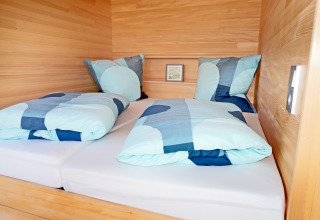 Modern twin bed with blue bedding in a wood-paneled cabin, photographed at Haus Wasser, Germany.