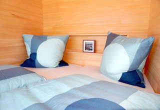 Cozy bed with blue bedding and pillows in a wooden cabin called Haus Wasser in Germany.