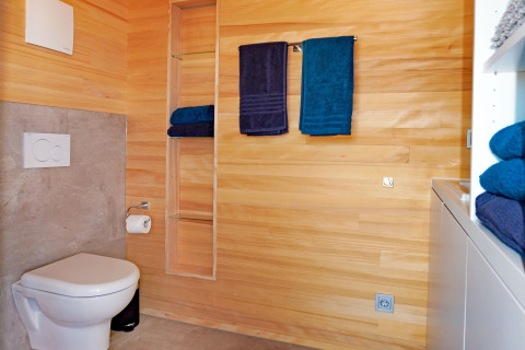 Modern wooden bathroom at Haus Wasser, Germany, featuring wall-mounted toilet and blue towels.
