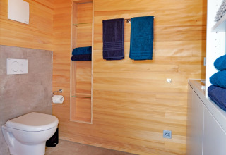 Modern wooden bathroom at Haus Wasser, Germany, featuring wall-mounted toilet and blue towels.