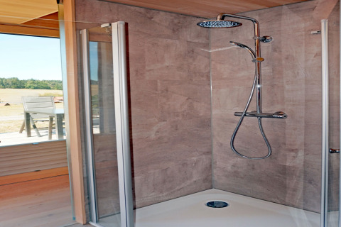 Modern shower cabin with glass doors and rainfall shower in Haus Wasser cabin, Germany, nature outside.