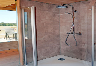 Modern shower cabin with glass doors and rainfall shower in Haus Wasser cabin, Germany, nature outside.