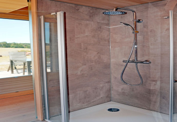 Modern shower cabin with glass doors and rainfall shower in Haus Wasser cabin, Germany, nature outside.