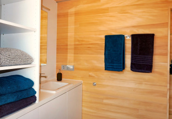 Moderne badkamer in Haus Wasser, Duitsland, met houten wanden en keurig opgeruimde gekleurde handdoeken.