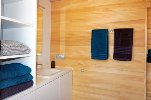 Modern bathroom at Haus Wasser in Germany featuring wood-paneled walls and neatly arranged towels.