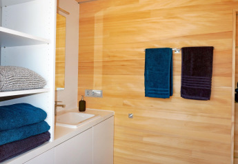 Modern bathroom at Haus Wasser in Germany featuring wood-paneled walls and neatly arranged towels.
