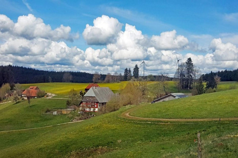 Scenic countryside at Haus Wasser, Germany, with green hills, farmhouses, wind turbines, and a blue sky.