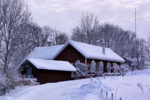 Snow-covered cabin named Haus Wasser in Germany, nestled among leafless trees and a wintry landscape.