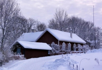 Snow-covered cabin named Haus Wasser in Germany, nestled among leafless trees and a wintry landscape.