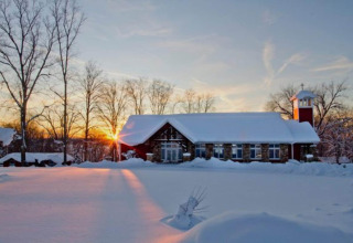 Snow-covered cabin named Haus Wasser in Germany, with sunset and winter landscape in the background.