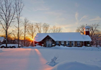 Snow-covered cabin named Haus Wasser in Germany, with sunset and winter landscape in the background.
