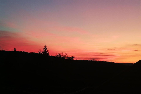 Stunning sunset sky with vibrant colors seen from the cabin Haus Wasser in Germany, trees in silhouette.