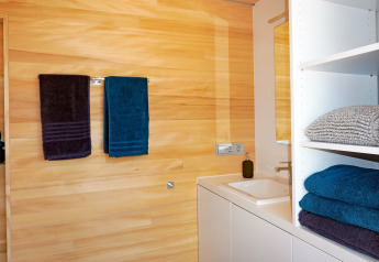 Modern bathroom with light wood walls, white shelves, and colorful towels at Haus Wasser cabin in Germany.