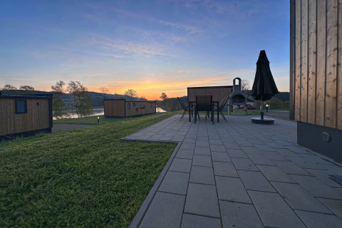 Blick auf Tiny Chalets am Eixendorfer See in Deutschland bei Sonnenaufgang, mit Terrasse und Gartenmöbeln.