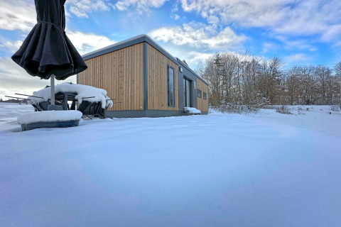 Klein houten chalet met besneeuwd terras bij Holiday village SEEBLICK, meer Eixendorfer, Duitsland.