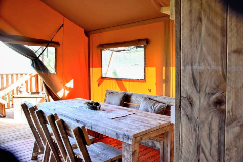 Interior of a safari tent with a rustic wooden table, chairs, orange canvas walls, and a window in daylight.