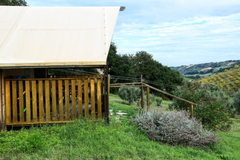 Safari tent with wooden deck, set in lush green countryside with scenic hills and fields in the background.