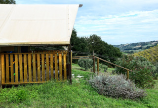 Safari tent with wooden deck, set in lush green countryside with scenic hills and fields in the background.