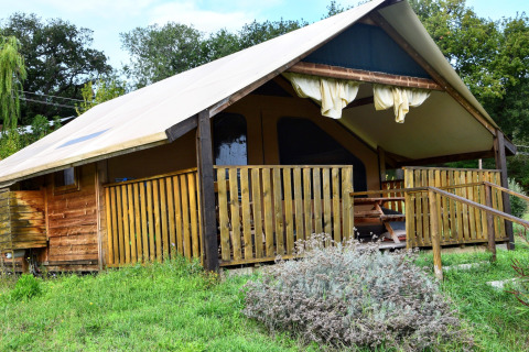Foto de una tienda safari con terraza de madera, situada sobre césped verde y rodeada de árboles.