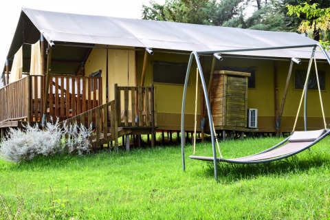 Tienda safari sobre césped verde con columpio tipo hamaca y terraza de madera, rodeada de naturaleza.