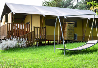 Tienda safari sobre césped verde con columpio tipo hamaca y terraza de madera, rodeada de naturaleza.