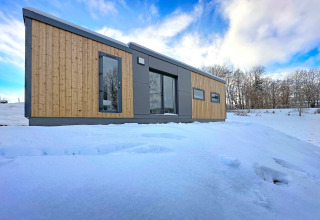 Tiny house moderne 'SEEBLICK - Tiny Chalet on Lake Eixendorfer' dans la neige, entourée d’arbres en Allemagne.