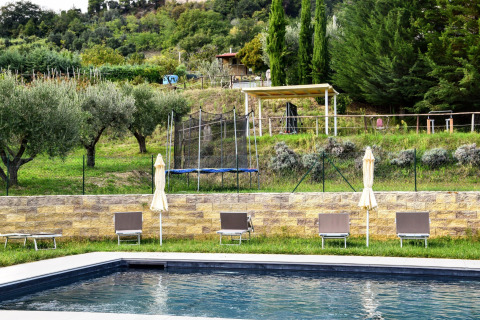 Swimming pool with sun loungers and umbrellas overlooking green hills at a safari tent campsite.