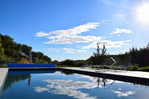 Outdoor swimming pool at a safari tent site with lounge chairs, blue sky, sun, and tranquil scenery.