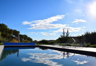 Piscina al aire libre en un campamento de tienda safari con tumbonas, cielo azul y ambiente soleado.