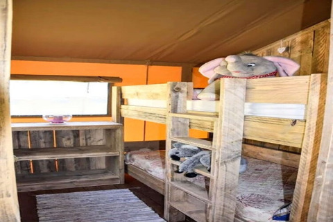 Safari tent kids' room with wooden bunk beds, stuffed animals, rustic shelf unit, and light from window.