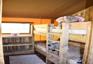 Safari tent kids' room with wooden bunk beds, stuffed animals, rustic shelf unit, and light from window.