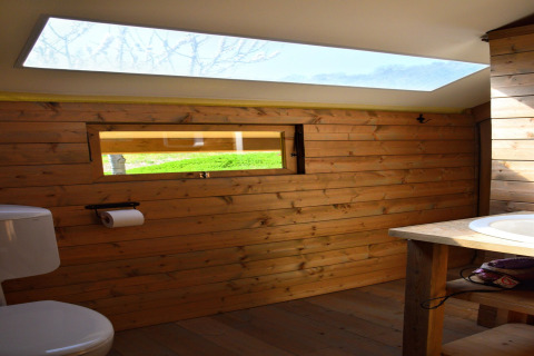 Safari tent bathroom with wooden walls, skylight, window, toilet, and sink, featuring natural light.
