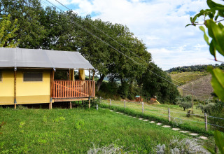 View of the luxury safari tent ‘Tenda Luxury 1’ with a terrace overlooking green fields in Italy.